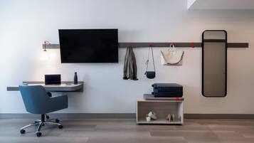 A modern hotel room with a desk, chair, TV, and a shoe rack.