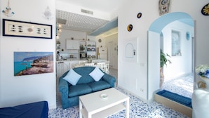 A compact living space with a sofa, a coffee table, and a kitchen area visible through an open doorway.