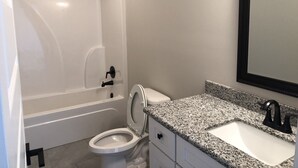 Een badkamer met een wit bad, toilet en een wastafel met granieten blad.