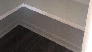Een hoek van een kamer met drie witte planken tegen een grijze muur.