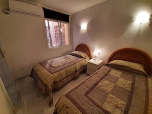 Et soveværelse med to senge, et natbord med lampe, et vindue med udsigt og en aircondition.