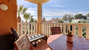 Een balkon met een houten tafel, twee stoelen, een bankje en een cactus in een pot.