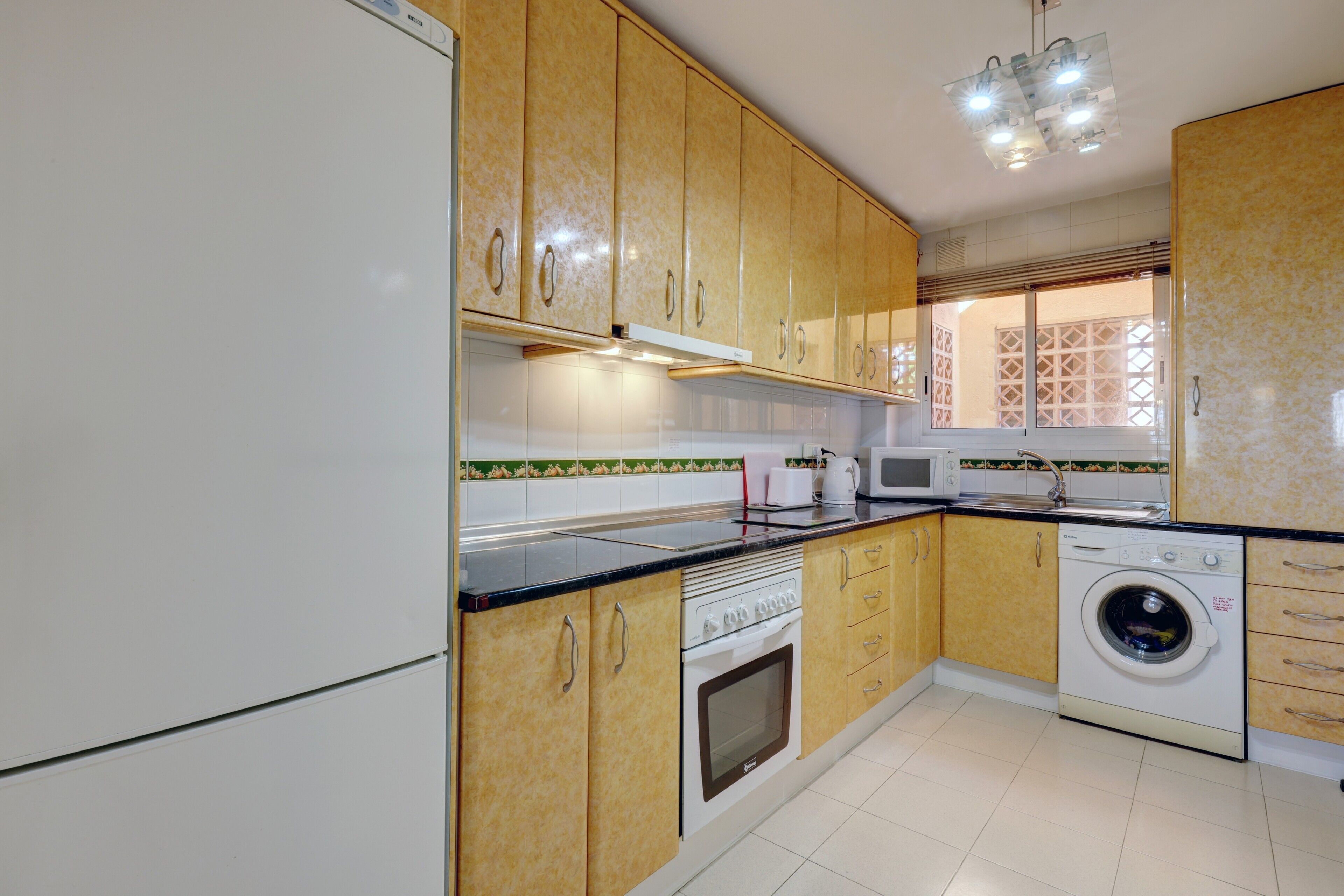 Een keuken met houten kastjes, een magnetron, een oven en een wasmachine.