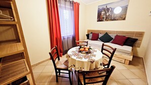 A dining area with a round table, chairs, and a bowl of fruit. There is a sofa with cushions and a wall-mounted picture. - Country House near Rome (Castel Madama)