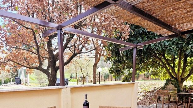 An outdoor patio with a table and wicker chairs, a bowl of oranges, and a bottle of wine. - Country House near Rome (Castel Madama)