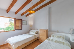 Une chambre avec deux lits simples, des poutres en bois, une fenêtre, une lampe fixée au mur et une petite plante.