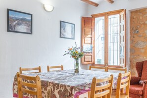 Un comedor con una mesa redonda, sillas, un florero con flores y dos cuadros en la pared.