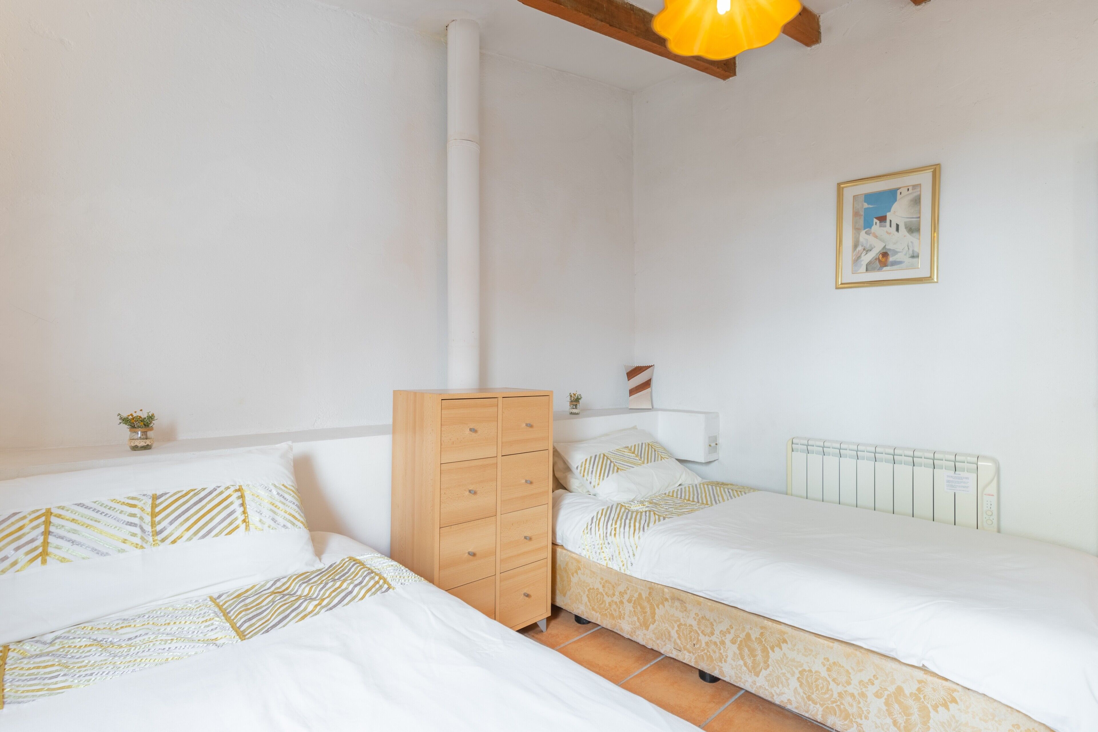 A bedroom with two beds, a wooden dresser, a radiator, and a framed picture on the wall.