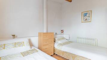 A bedroom with two beds, a wooden dresser, a radiator, and a framed picture on the wall.