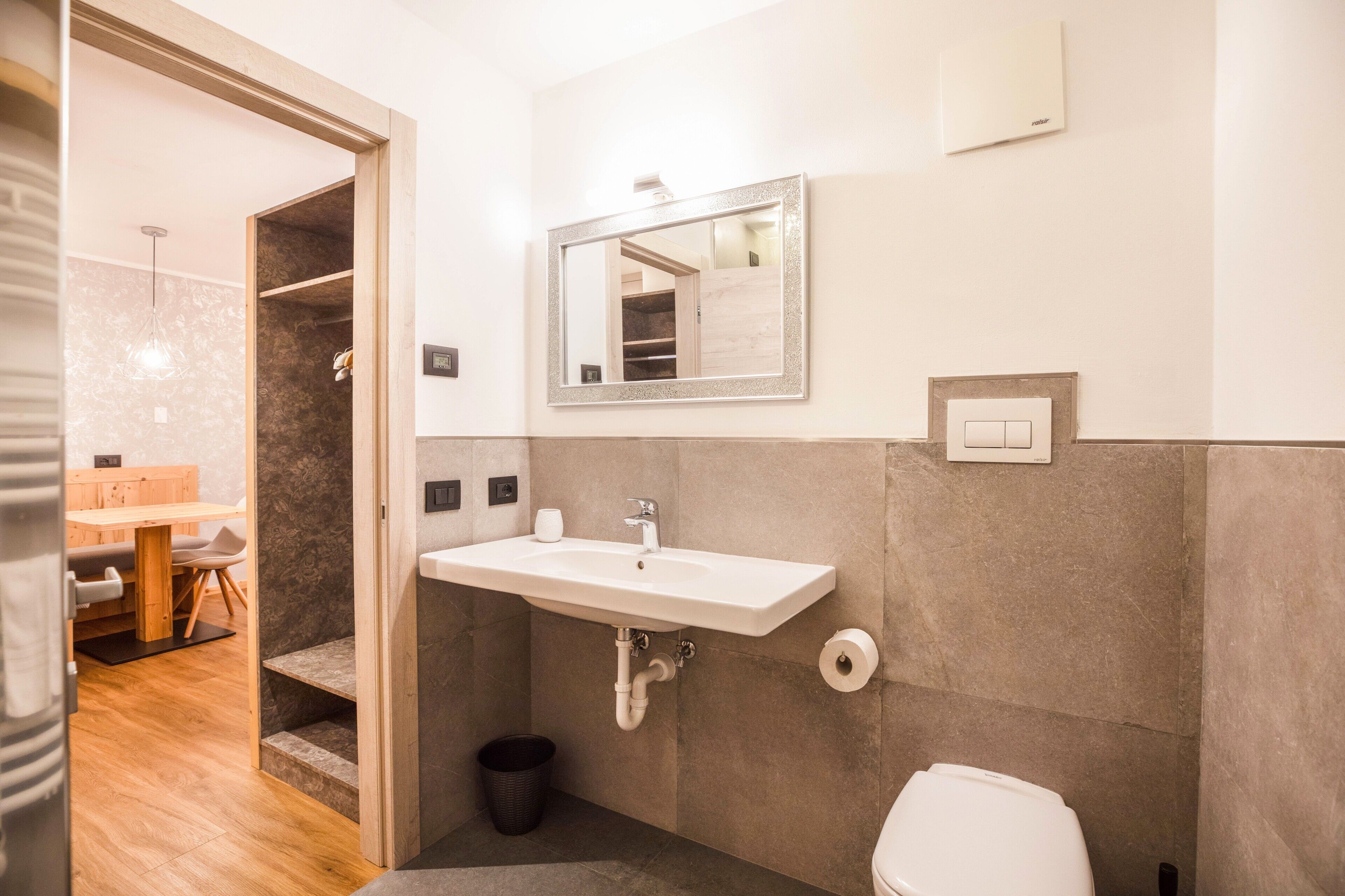 A bathroom with a sink, mirror, toilet, and a small trash bin.
