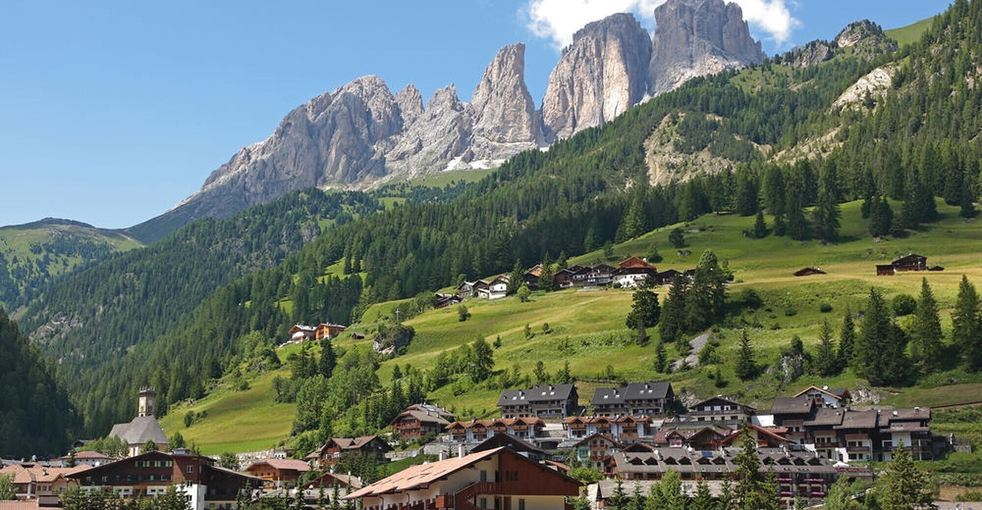 A mountain village with traditional houses, a church, and a prominent mountain range in the background.