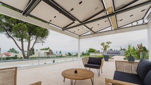 A spacious outdoor patio with a round wooden table, wicker furniture, and potted plants. - Holiday Home "Lagolino Boutiquehouse " with Pool, Garden & Wi-Fi (Pacengo/Lazise)