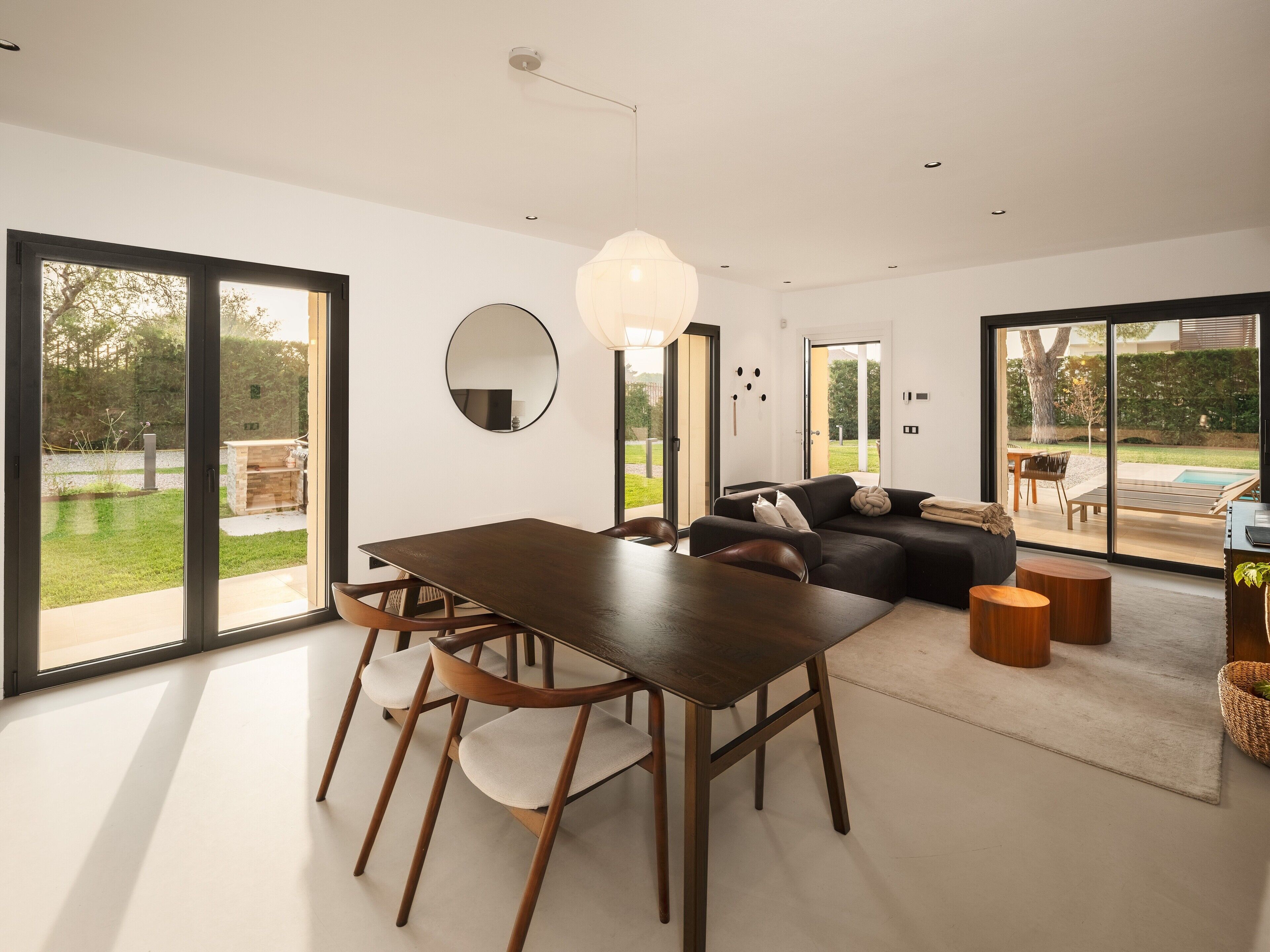 Un interior moderno con comedor, sofá y grandes puertas correderas de vidrio a un jardín.