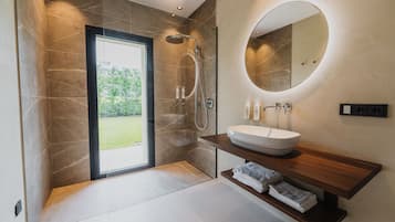 Ein modernes Badezimmer mit einer großen Badewanne, einem runden Spiegel und einer Dusche.