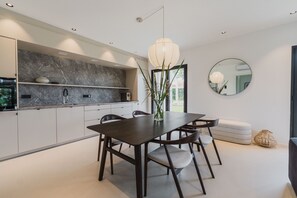 A modern kitchen with dark cabinetry, a marble backsplash, and a dining area with a dark wooden table and chairs.