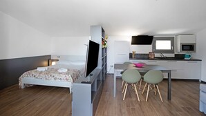 Habitación compacta con cama, televisión, escritorio con sillas, kitchenette y ventana.