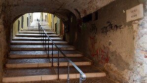 Una escalera con barandillas metálicas que asciende a través de una estructura parecida a un túnel, con un letrero que dice 'VICOLO MANINI'.