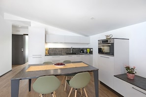 Une cuisine moderne avec des meubles blancs, une table à manger avec des chaises et un petit îlot central agrémenté d’une plante.