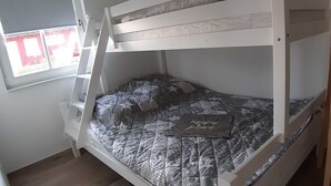 Una cama litera con colchón acolchado, una ventana con persianas y un suelo de madera.
