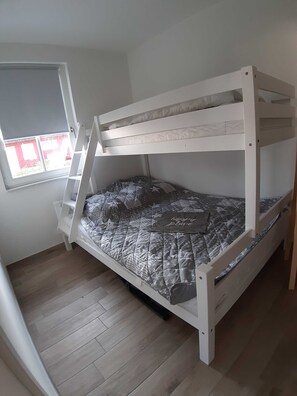 Un lit superposé avec un matelas matelassé, une fenêtre avec des stores et un plancher en bois.