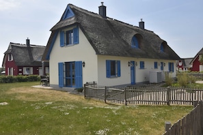 Une maison traditionnelle avec un toit de chaume, des volets bleus et une clôture en bois.