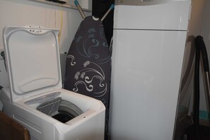Un espace buanderie compact comprenant un lave-linge, un fer à repasser et un réfrigérateur.