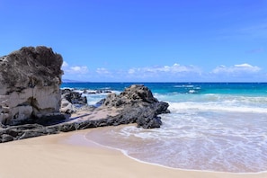 Ein Strand mit klarem, blauem Wasser, Felsformationen und einem Sandstrand.