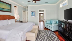A bedroom with a large bed, a ceiling fan, a TV, a light blue sofa, and a patterned rug.