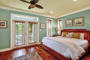Une chambre à coucher avec un lit en bois, un ventilateur de plafond et une grande fenêtre équipée de stores.