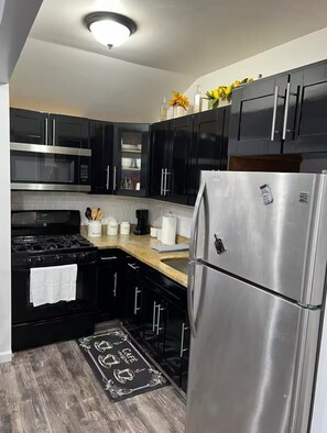 A modern kitchen with black cabinets, stainless steel appliances, and a granite countertop. - Cozy 1Bedroom Lower Level Apt (Saint Albans)
