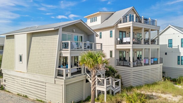 Ein zweistöckiges Strandhaus mit Balkon, einer kleinen Terrasse und einer Palme.