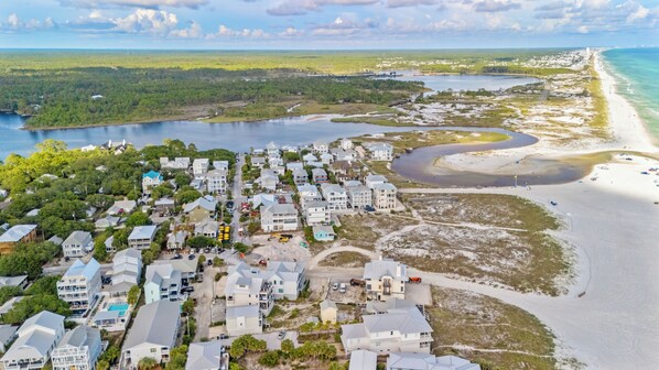 An aerial view of a coastal residential area with houses, a beach, and a river.