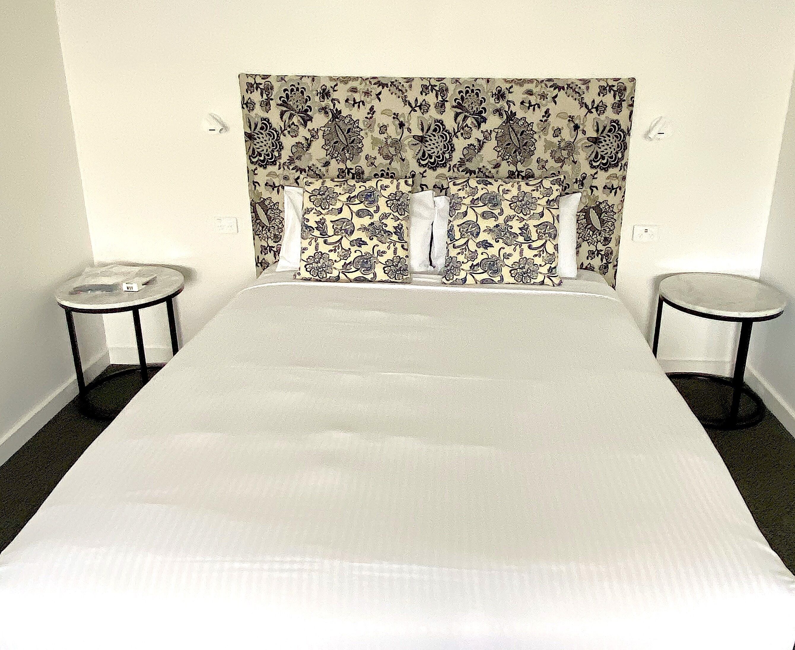 A hotel room with a large bed, two small side tables, and a patterned headboard.
