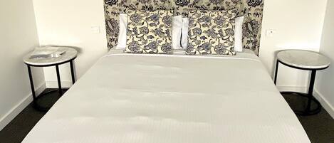 A hotel room with a large bed, two small side tables, and a patterned headboard.