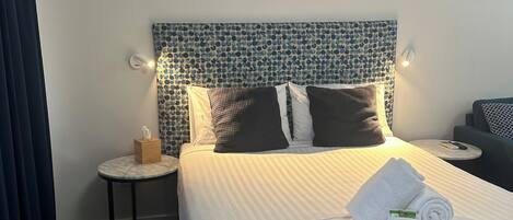 Ein Hotelzimmer mit einem Bett, einem Kopfstück mit blauem Muster, einem Nachttisch mit Taschentuchbox und einem kleinen runden Tisch mit Fernbedienung.