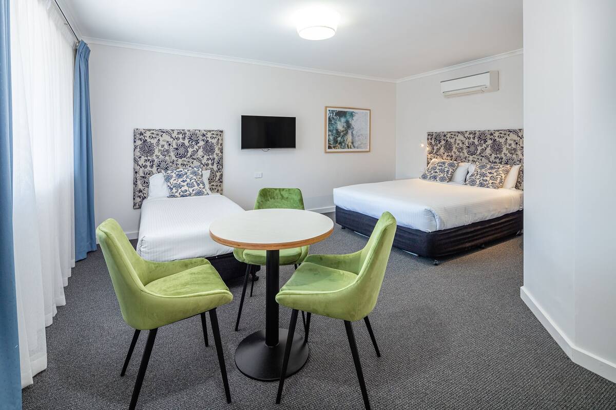 A hotel room with a bed, a TV, a painting, and a table with chairs.