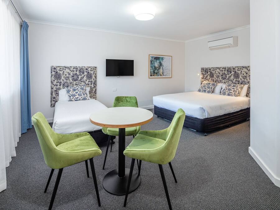 A hotel room with a bed, a TV, a painting, and a table with chairs.