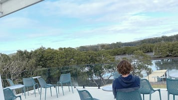 A balcony with chairs and a table, overlooking a lake and trees.