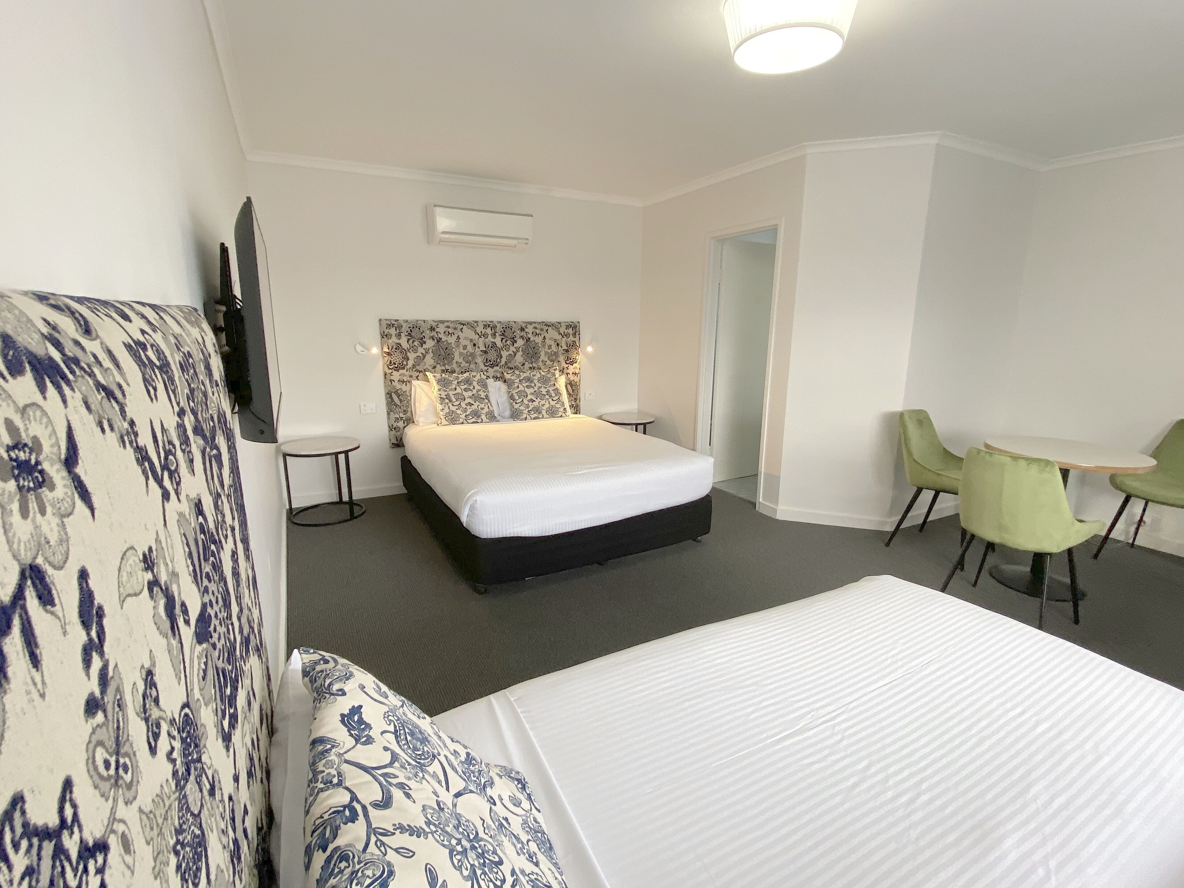 A hotel room with a large bed, a small round table, two green chairs, and a patterned sofa.