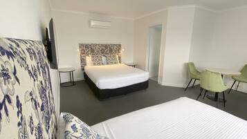 A hotel room with a large bed, a small round table, two green chairs, and a patterned sofa.