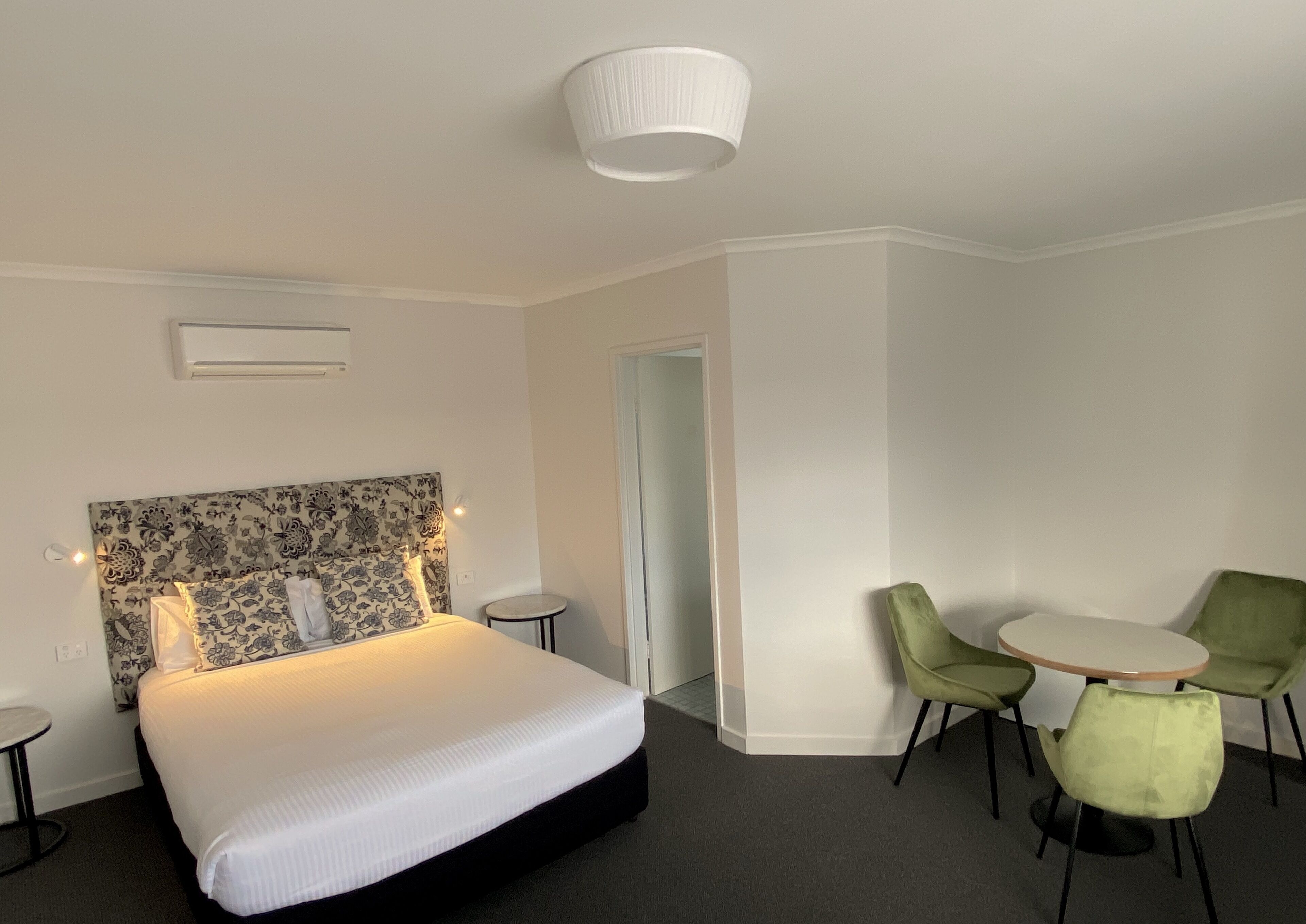 A hotel room with a bed, a small round table, two chairs, and a door leading to another room.