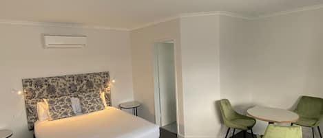 A hotel room with a bed, a small round table, two chairs, and a door leading to another room.