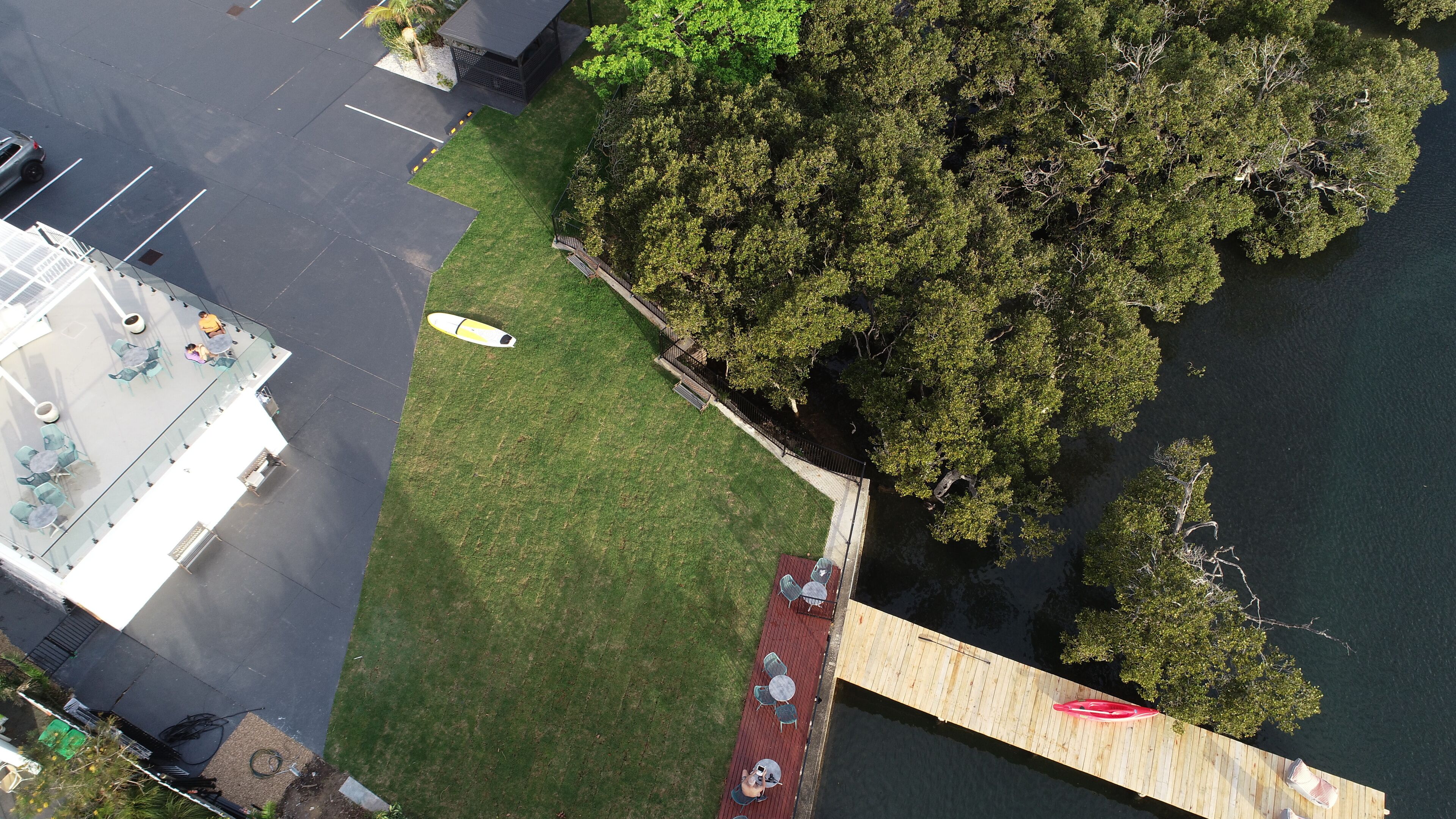 An aerial view of a waterfront property with a wooden dock, grassy areas, and a parking lot.