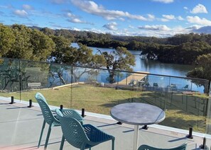 A terrace with a table and chairs overlooking a lake and forested hills. - Batemans Bay Lodge (Batemans Bay)