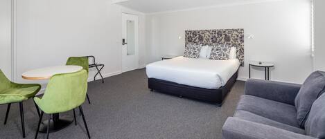 A hotel room with a bed, a grey sofa, a green chair, a small round table, and a white door.