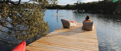 A wooden dock extending into calm water, with a red kayak and two cushioned chairs on the dock.