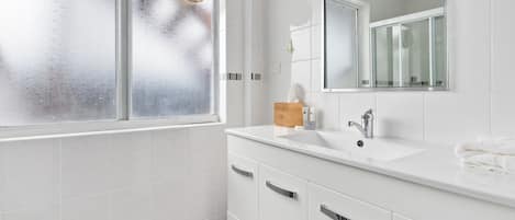 Un baño con lavamanos, espejo y armarios blancos.