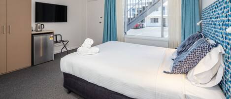 Ein Hotelzimmer mit Bett, Schreibtisch mit Wasserkocher, Fernseher und Blick auf ein Gebäude mit einer Treppe.
