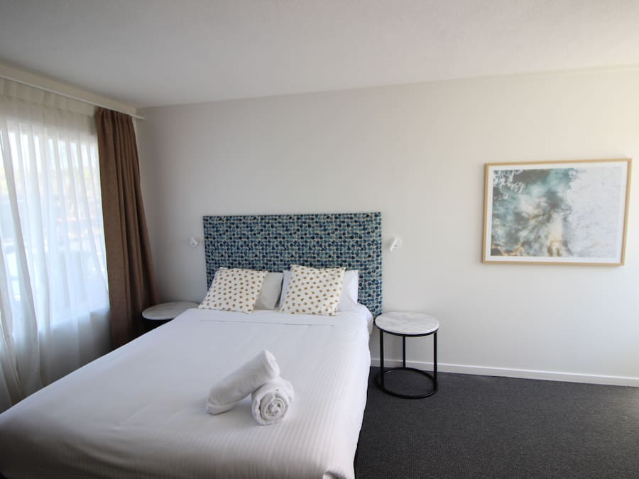 A hotel room with a large bed, a headboard with a blue pattern, a round side table, and a framed picture on the wall.