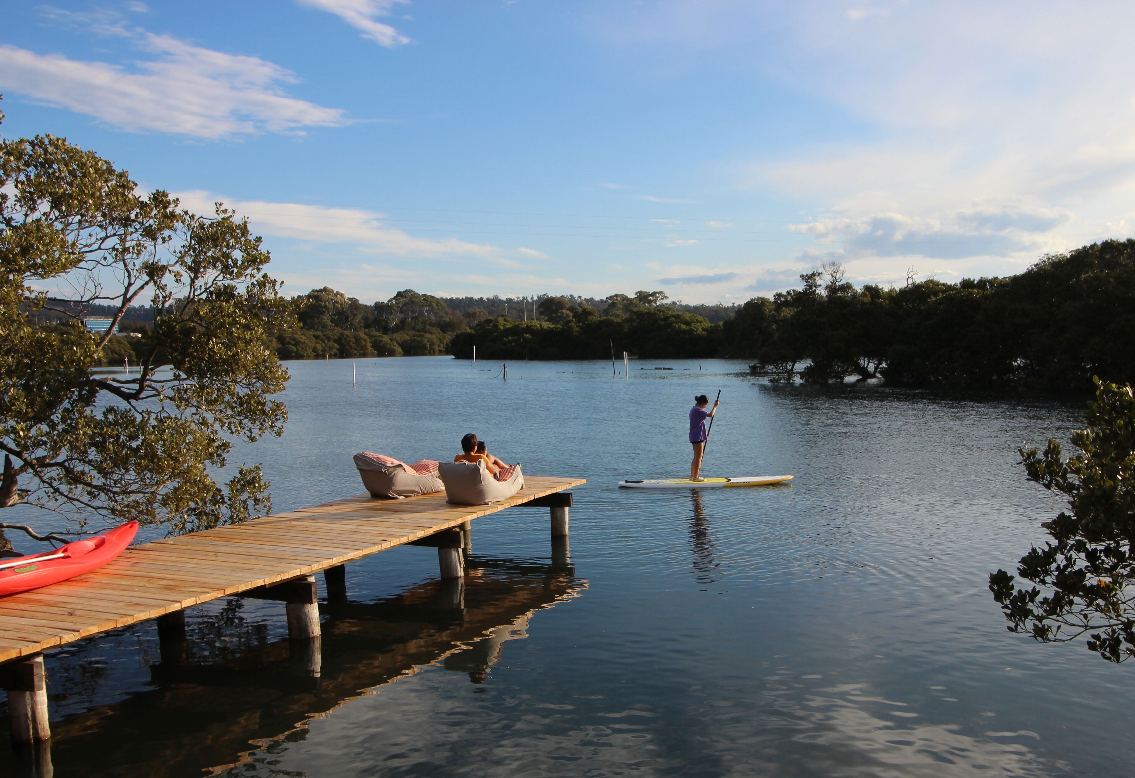 A wooden dock extending into calm water with a kayak and paddleboarder.